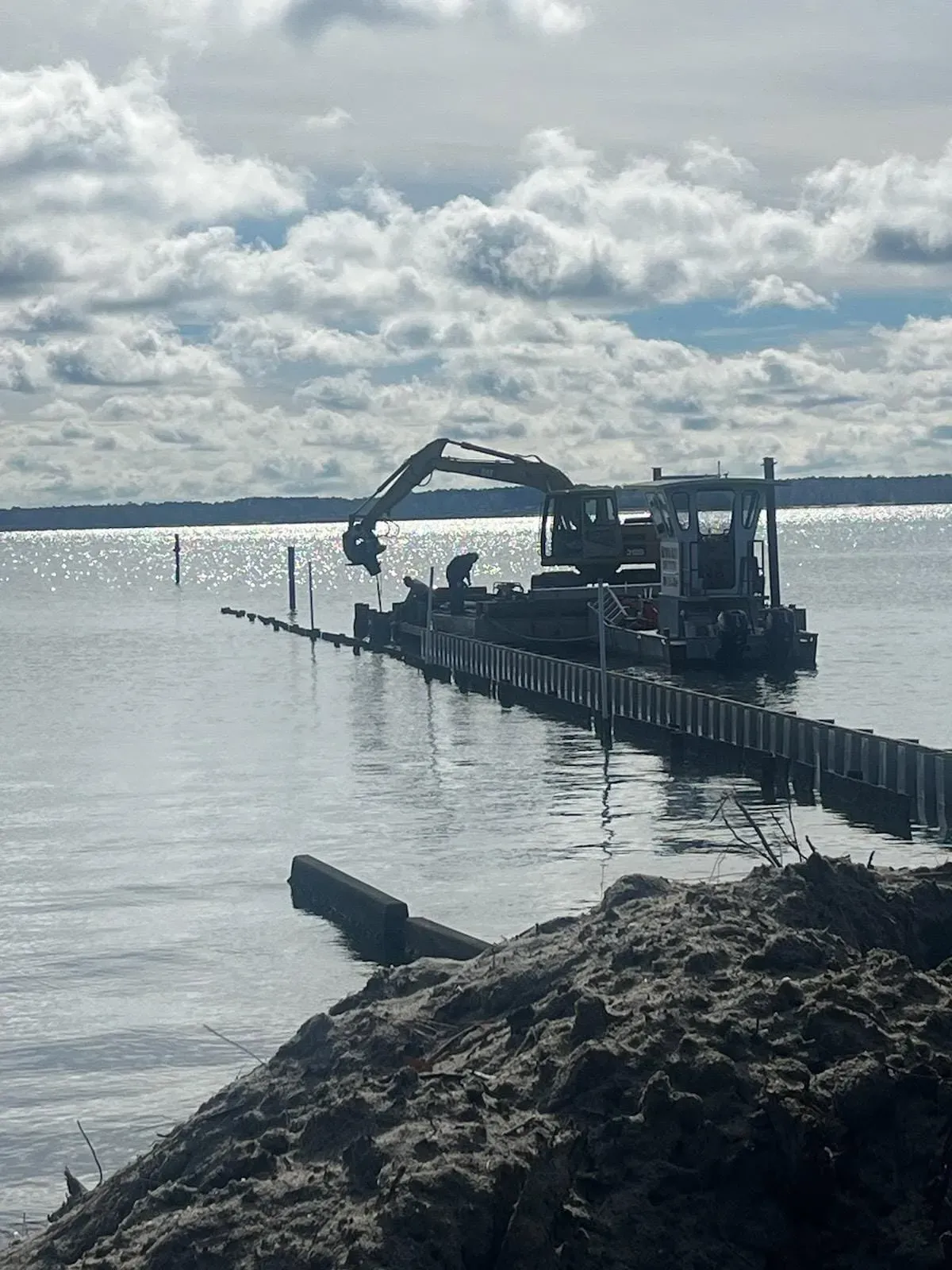 Excavator barge working on the bay under clouds