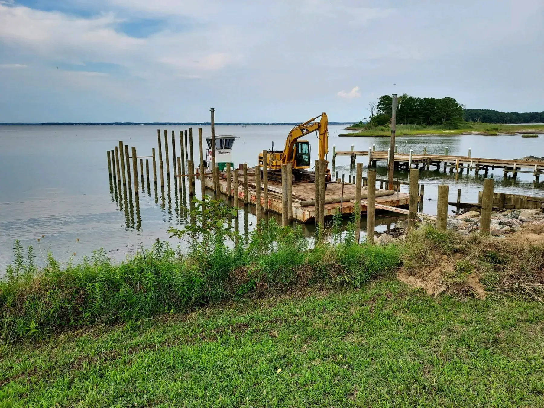 Barge and new pilings off a grassy shoreline