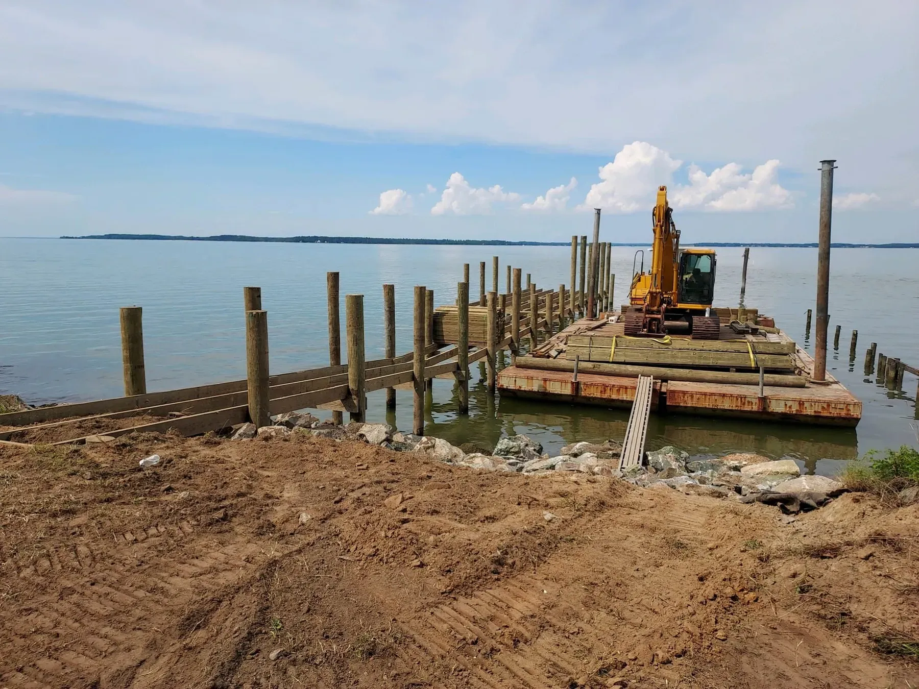 The same pier during construction, with the excavator on the barge setting pilings