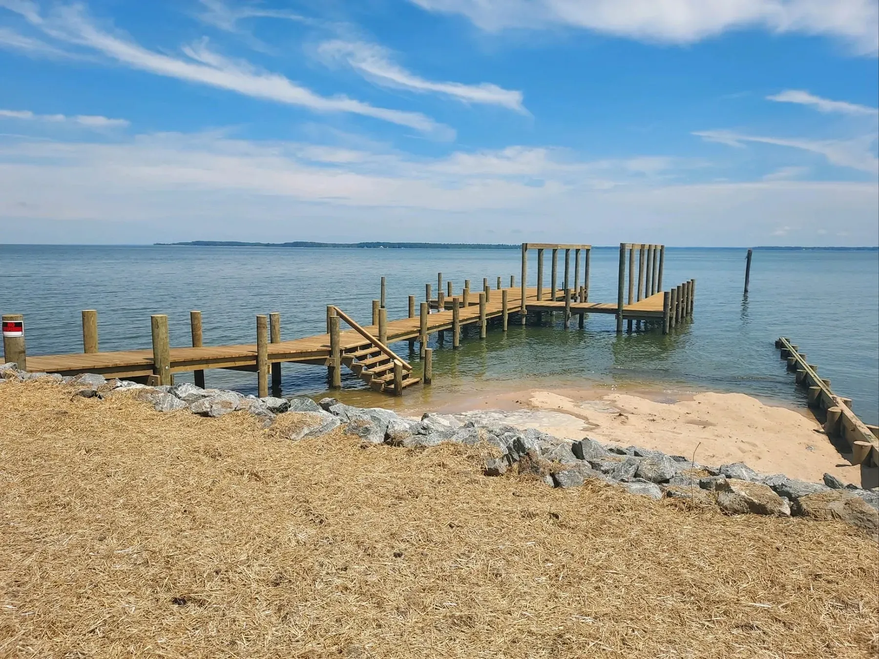 Finished bayfront pier with stairs down to a sandy beach and stone rip-rap