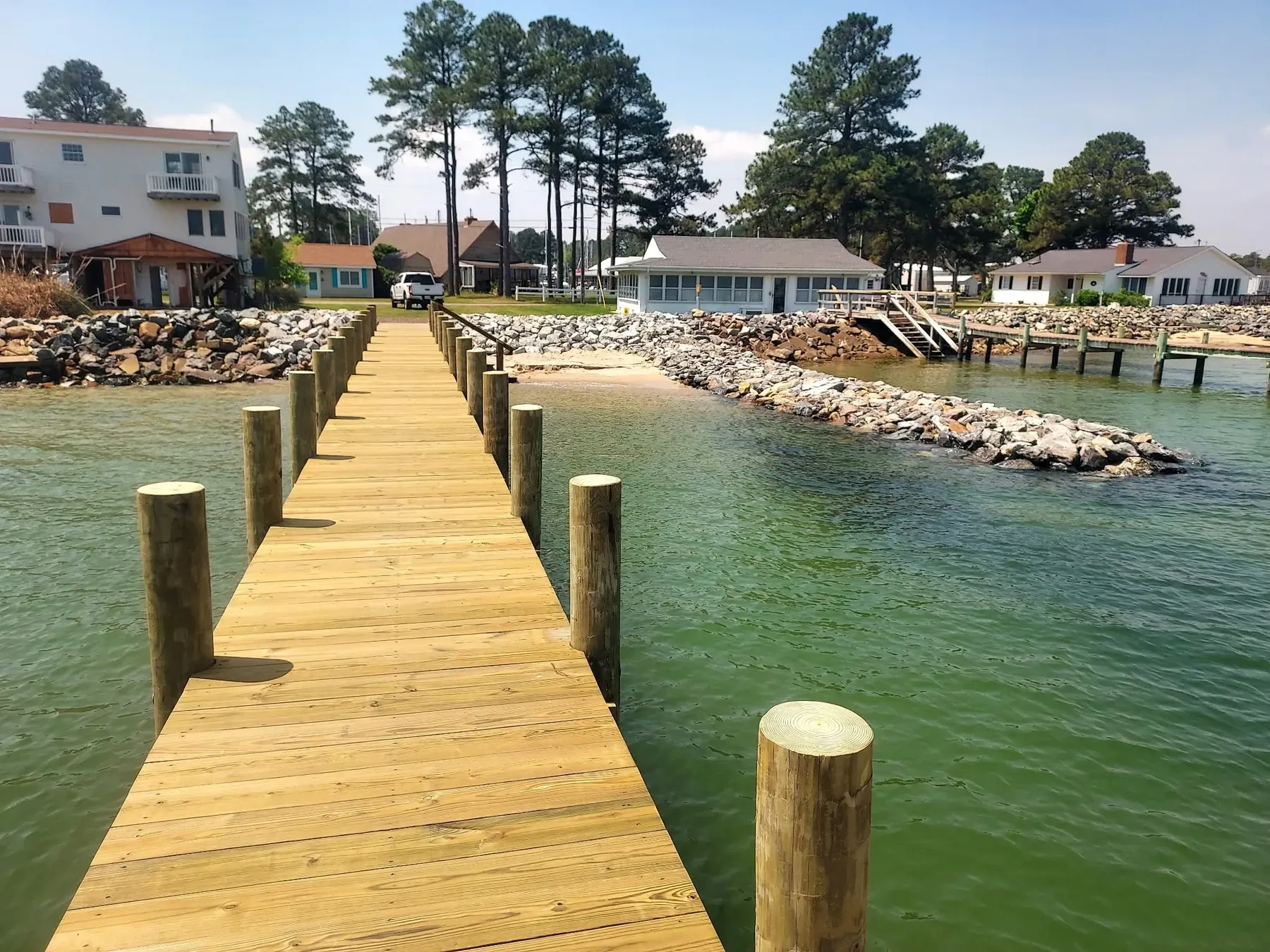 New Haywood Marine pier running straight out between stone rip-rap, with waterfront homes and pines on the shore